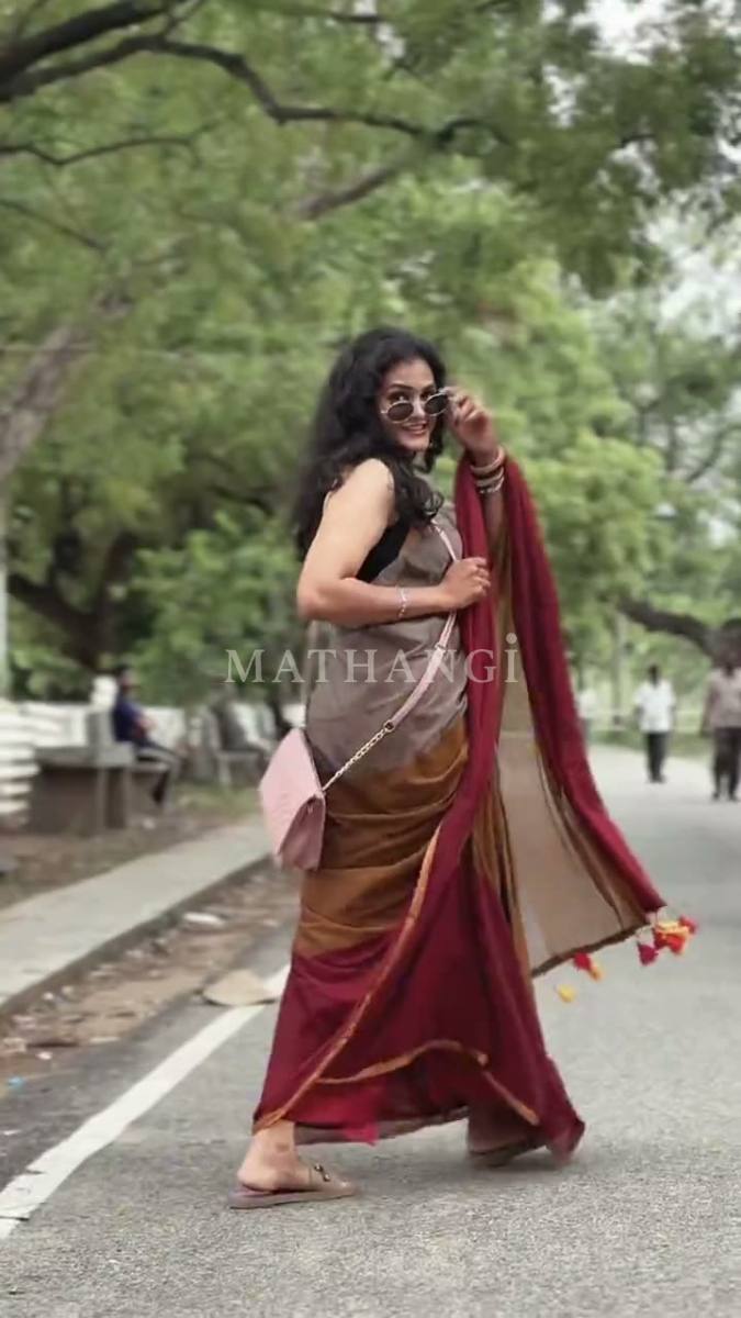 A tan and maroon saree with tassels at the pallu, worn walking a tree-lined road