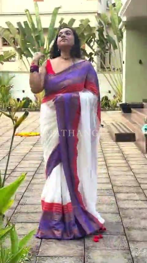 A white saree with a purple and gold border and a red line along it, worn in a garden courtyard