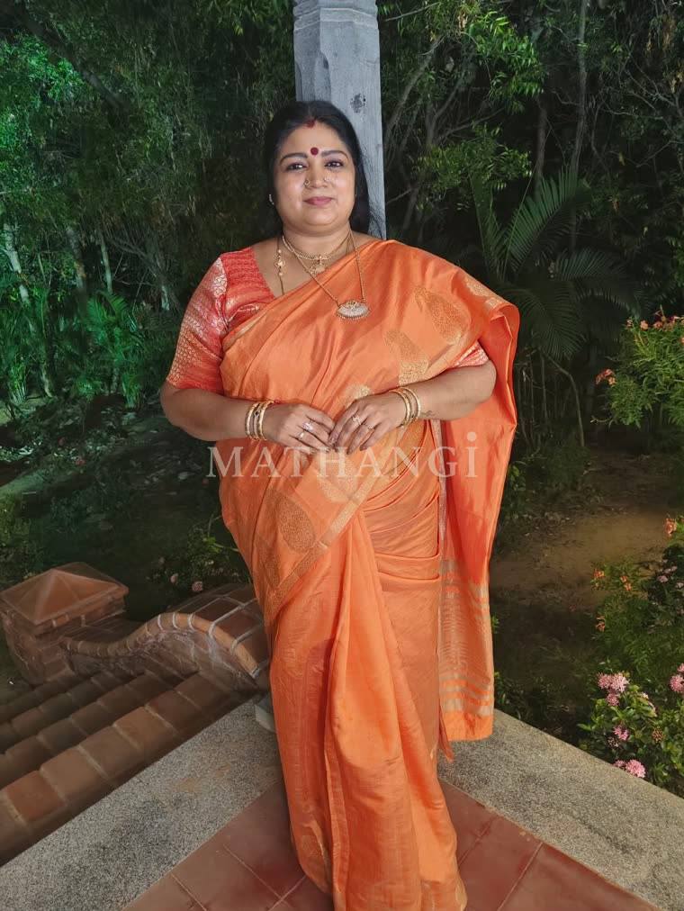 An orange saree with gold buttas and a gold border, worn on a garden step
