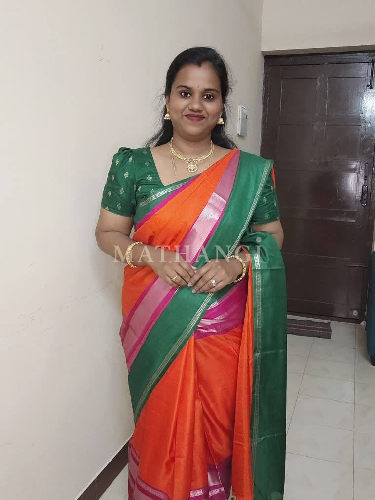 An orange saree with a green border and pink and silver bands, worn in a house hallway