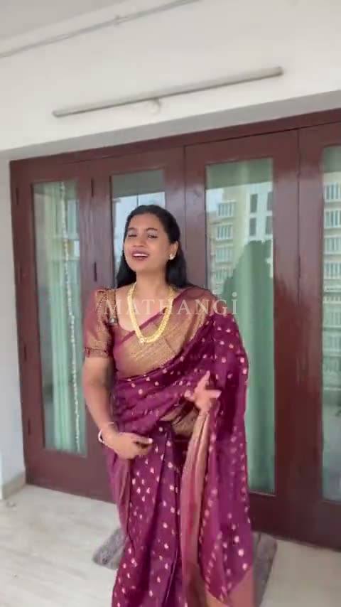 A wine saree with small gold buttas and a broad gold border, worn in a doorway