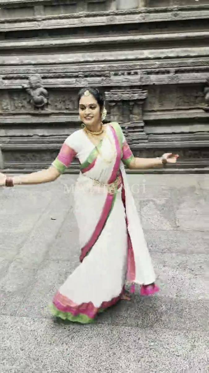A white saree with a pink and green border and pink tassels, worn at a stone temple