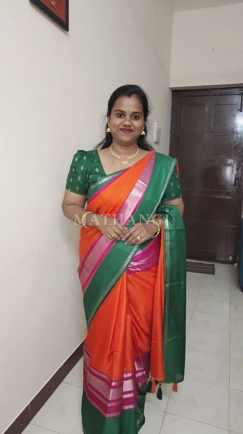 An orange saree with a green border and pink and silver bands, worn in a house hallway